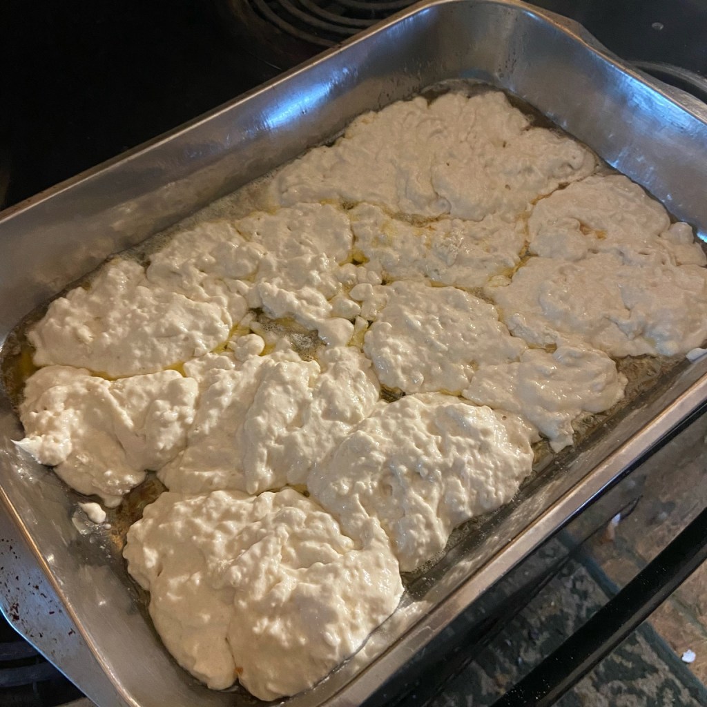Cobbler batter spooned over melted butter in a baking dish, ready for peaches.