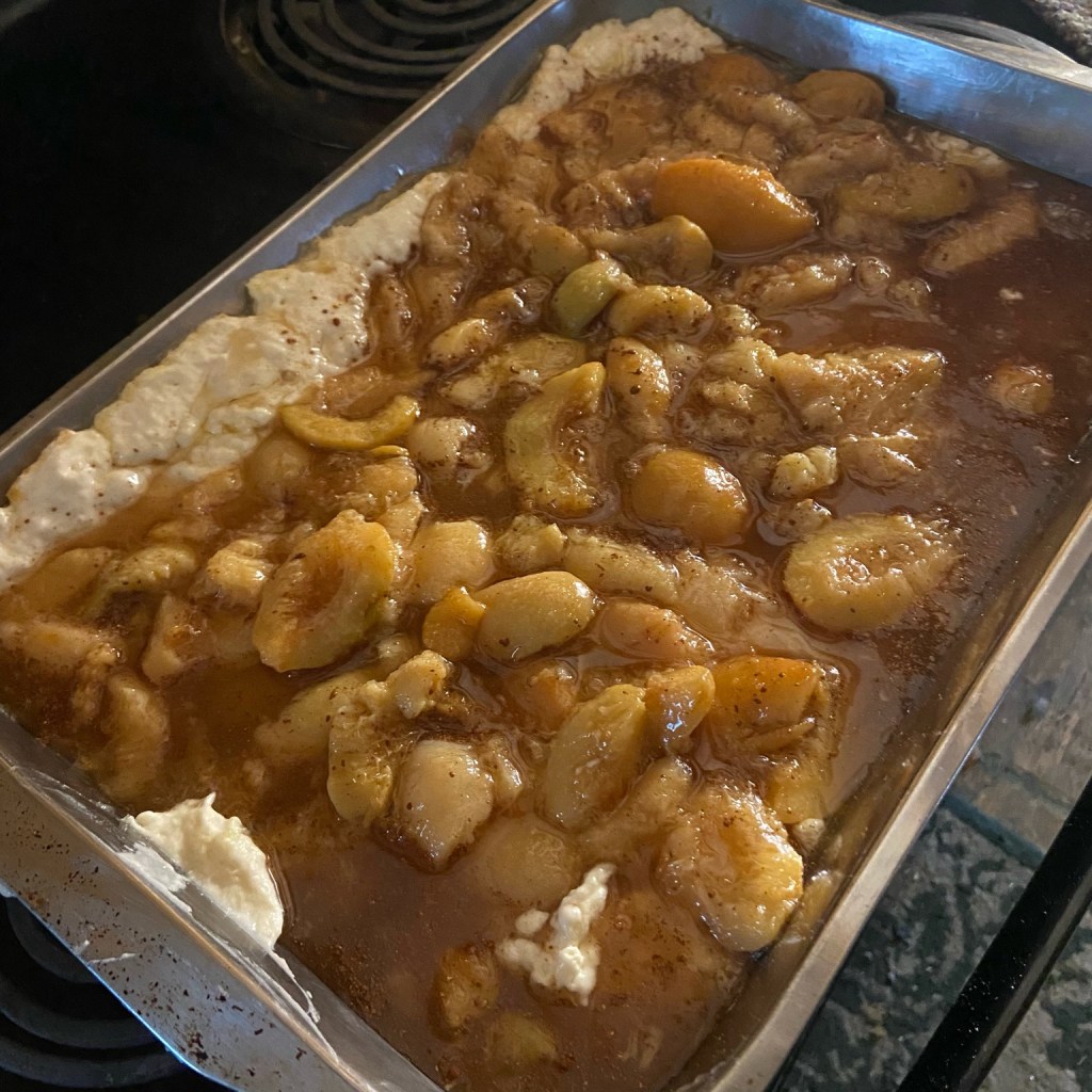 Unbaked peach cobbler with batter and fruit layered in a pan.