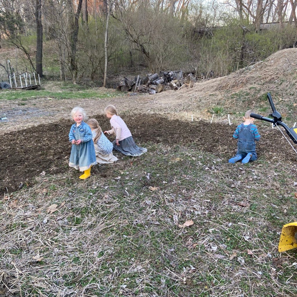 Four small children planting seeds and digging in a garden bed on a spring day.